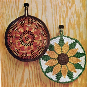 May include: Two crocheted pot holders hanging on a wooden wall. One is a brown and orange floral design, the other is a green, white, and yellow sunflower design.