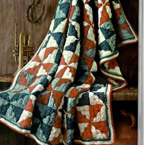 Könnte beinhalten: Eine gehäkelte Decke mit Patchwork-Muster in Rot-, Weiß-, Blau- und Grüntönen. Die Decke ist gefaltet und über eine Holzoberfläche gelegt.