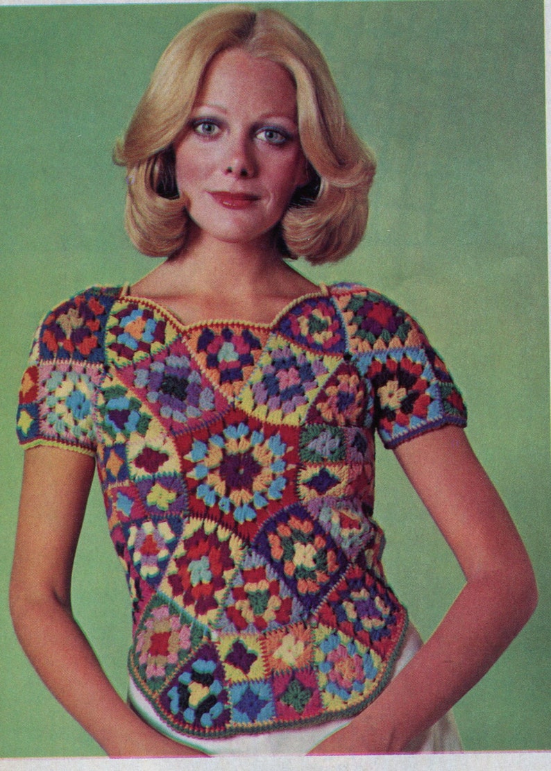 May include: A woman wearing a colourful crochet top with a square pattern. The top has short sleeves and a scoop neck.