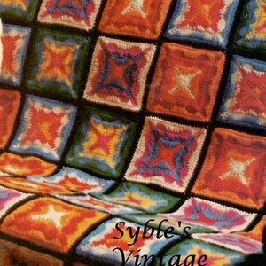 May include: A colourful crocheted blanket with a square pattern in shades of red, orange, yellow, green, blue, and white. The blanket is folded in half and the text "Syble's Vintage Patterns" is visible in the lower right corner.