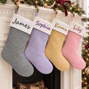 May include: Four Christmas stockings with a gingham pattern in black, purple, yellow, and pink. Each stocking features a white cuff with embroidered names: James in black, Sophia in purple, Emma in gold, and Lily in pink, hanging from gold hooks.