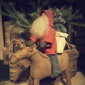 May include: A handmade felt Santa Claus doll riding a brown felt reindeer. The Santa doll is wearing a red coat with a white beard and a white fur trim. The reindeer has brown antlers and a brown felt body.