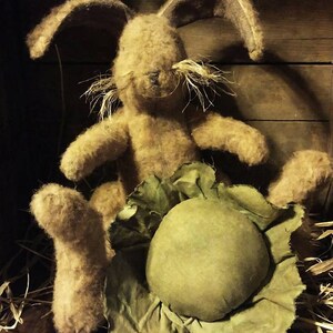 May include: A brown, fuzzy bunny rabbit sits in a green cabbage with a ruffled edge. The bunny has long ears and a long, white mustache. The bunny is sitting in a wooden box with straw on the bottom.