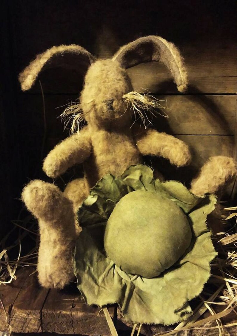 May include: A brown, fuzzy bunny rabbit sits in a green cabbage with a ruffled edge. The bunny has long ears and a long, white mustache. The bunny is sitting in a wooden box with straw on the bottom.