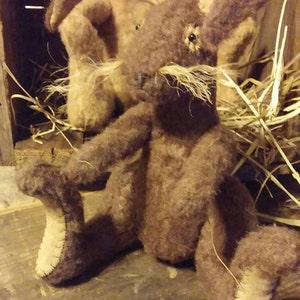 May include: A brown plush rabbit toy with long ears and a stitched nose. The rabbit is sitting on a wooden surface with straw in the background.