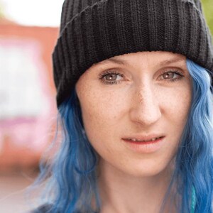 May include: A solid black knit beanie with a ribbed texture and a folded cuff. The hat is constructed from a thick, dark yarn and features a vertical pattern throughout the fabric, providing a consistent look across the entire surface.