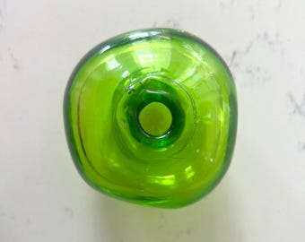 May include: A top-down view of a vibrant, translucent lime green glass bottle. The bottle features a rounded, organic shape with a smooth, polished surface and a circular opening at the center, showcasing the clear, bright green glass material.