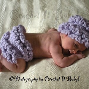 May include: A baby wearing a lavender crocheted hat and matching diaper cover. The hat has a ruffled edge and the diaper cover has a ruffled trim. The baby is lying on a white blanket.