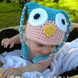 May include: A pink and blue crocheted owl hat with white and black eyes and a yellow beak. The hat has long ties that are pink and blue. The hat is on a baby's head.