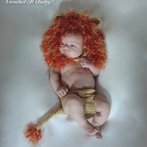 May include: A baby wearing a crocheted lion costume, including a fluffy orange and brown mane, ears, and a matching diaper with a tail. The text "A. Hertz © Crochet It Baby!" is in the upper left corner.