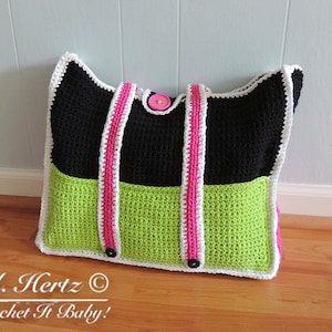 Op de afbeelding: Een zwarte en groene gehaakte tote bag met witte bies en roze banden. De tas heeft drie grote knoppen.