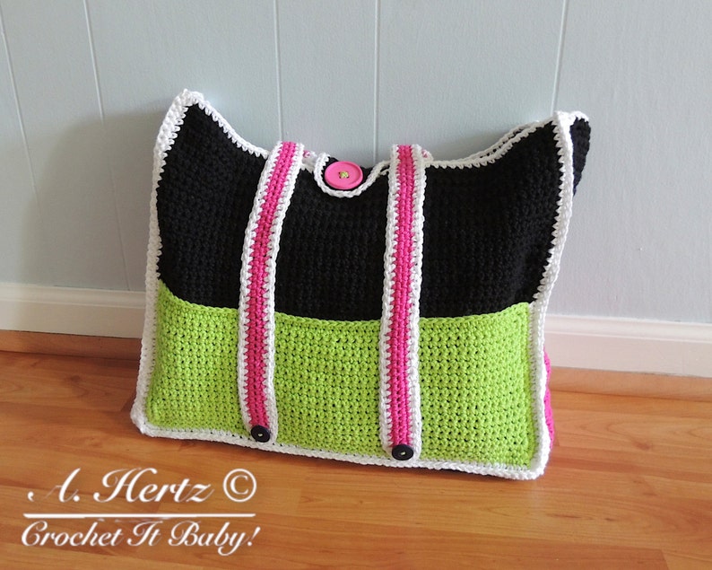 Op de afbeelding: Een zwarte en groene gehaakte tote bag met witte bies en roze banden. De tas heeft drie grote knoppen.