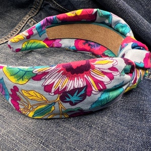 May include: A blue headband with a floral print featuring pink, yellow, green, and red flowers. The headband is tied in a knot on one side.