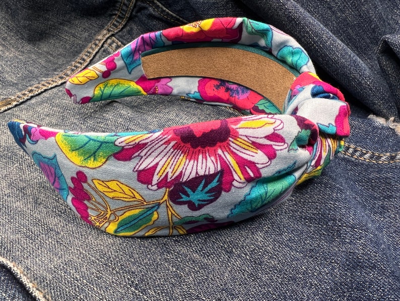 May include: A blue headband with a floral print featuring pink, yellow, green, and red flowers. The headband is tied in a knot on one side.