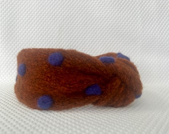May include: A brown fuzzy headband with blue polka dots. The headband is knotted on top.