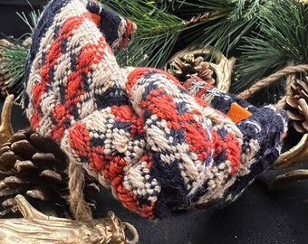 May include: A close-up of a knitted scarf with a plaid pattern in shades of red, white, and blue. The scarf is folded and draped over a decorative branch.