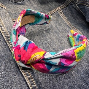 May include: A knotted headband with a floral print featuring pink, blue, yellow, and green flowers on a light blue background.