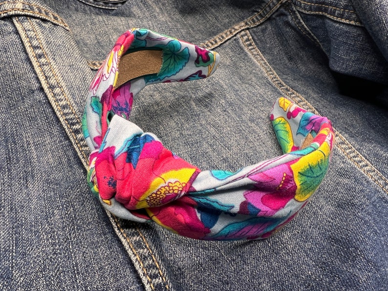 May include: A knotted headband with a floral print featuring pink, blue, yellow, and green flowers on a light blue background.