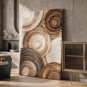 Puede incluir: Un cuadro rectangular sobre lienzo con una composición abstracta de formas circulares superpuestas en varios tonos de marrón, beige y crema, con pinceladas texturizadas visibles que crean un patrón de anillos concéntricos.