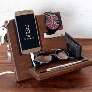 May include: A wooden organiser with compartments for a phone, watch, keys, sunglasses, and a pen. The phone is a Samsung Galaxy displaying the time as 19:20. The watch has a black strap and a red face with white markings. The organiser is made of dark brown wood.