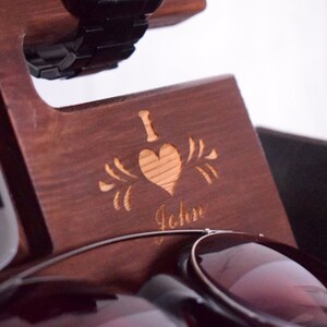 May include: A wooden organiser with a heart and the words "I love John" engraved on the front. The organiser has slots for a watch, phone, and sunglasses.
