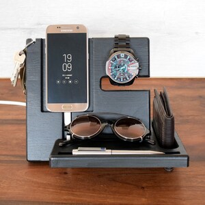 Puede incluir: Organizador de madera negro con ranuras para un tel&eacute;fono, un reloj, gafas de sol y una cartera. El tel&eacute;fono es un Samsung Galaxy con la hora 19:09 mostrada en la pantalla.
