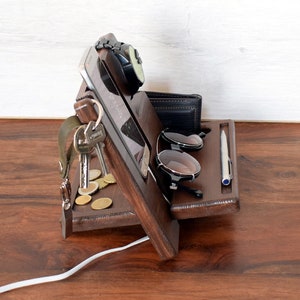 May include: Wooden organiser with compartments for a phone, watch, keys, sunglasses, and a pen. The organiser is made of dark brown wood and has a natural finish.