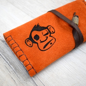Può includere: Borsa in pelle scamosciata arancione con un design di scimmia nera e un cinturino in pelle marrone.