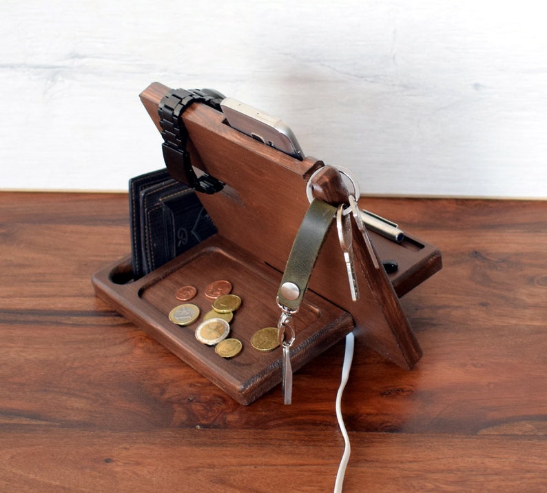 May include: Wooden organiser with compartments for a phone, watch, keys, and wallet. It has a tray for loose change and a slot for charging cables.