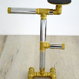 May include: A gold metal stand with a chrome pipe and a black round top. The stand has a base with four legs.