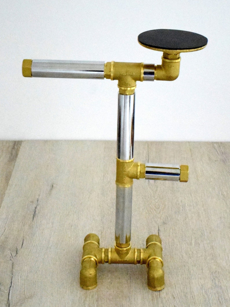 May include: A gold metal stand with a chrome pipe and a black round top. The stand has a base with four legs.