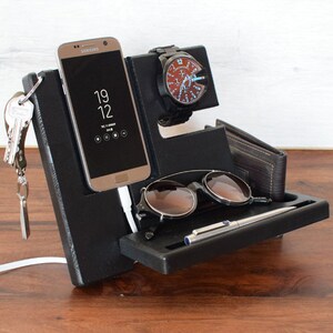 Puede incluir: Organizador de escritorio negro con compartimentos para un tel&eacute;fono, un reloj, gafas de sol y un bol&iacute;grafo. El organizador tiene un gancho para llaves y un cable de carga.