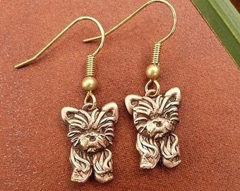 May include: A pair of gold-toned earrings featuring a small, detailed Yorkshire Terrier charm on each earring.
