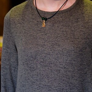 May include: A person wearing a dark green long-sleeved shirt with a black cord necklace and a small gold pendant.
