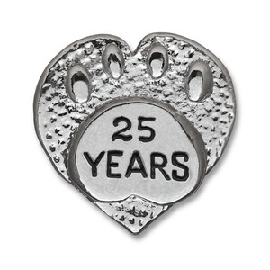 Puede incluir: Pin de plata en forma de coraz&oacute;n con un dise&ntilde;o de huella de pata y el texto "25 A&Ntilde;OS" dentro de la huella de pata.