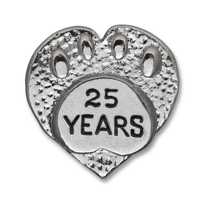 Puede incluir: Pin de plata en forma de coraz&oacute;n con un dise&ntilde;o de huella de pata y el texto "25 A&Ntilde;OS" dentro de la huella de pata.