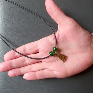 May include: A brown glass pendant shaped like a bear with green glass beads on a black cord necklace.
