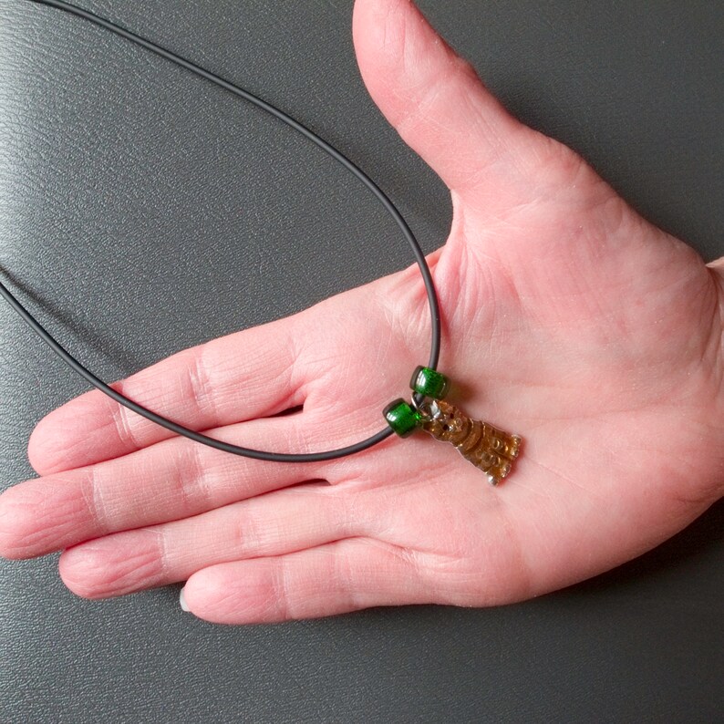 May include: A brown glass pendant shaped like a bear with green glass beads on a black cord necklace.