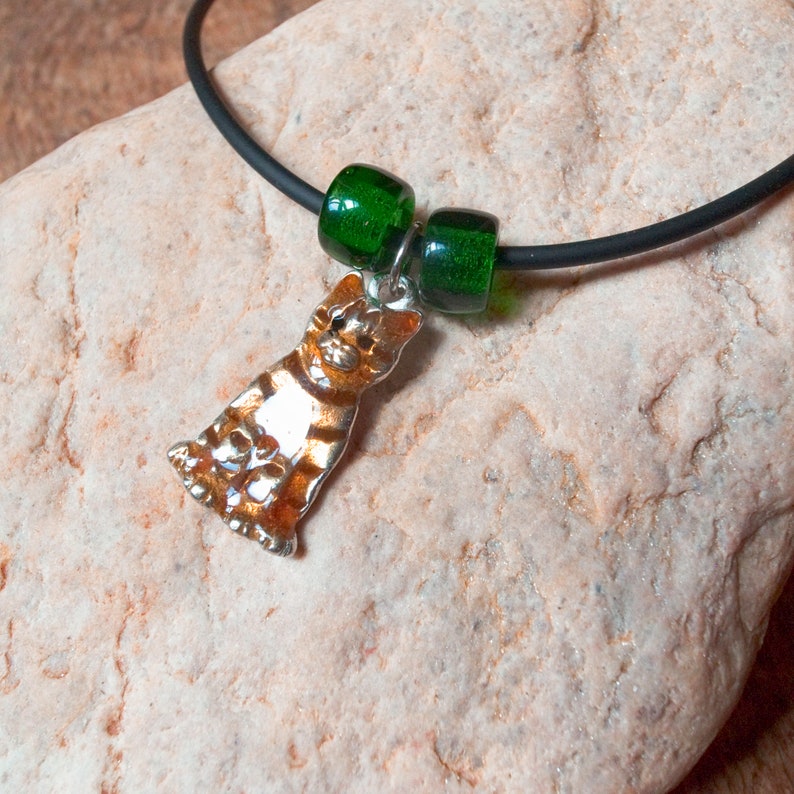 May include: A black choker necklace with a silver cat charm and two green glass beads.
