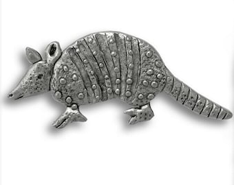 Könnte beinhalten: Eine silberfarbene Armadillo-Figur aus Zinn. Das Gürteltier ist in einer Gehpose dargestellt, wobei der Kopf nach links gedreht ist. Die Figur ist mit strukturierten Schuppen und einem strukturierten Körper detailliert.