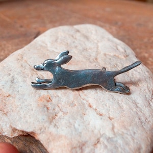 May include: A silver-toned brooch in the shape of a running dachshund.