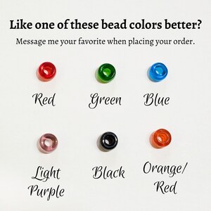 May include: Six round beads in different colours: red, green, blue, light purple, black, and orange/red. The text "Like one of these bead colours better? Message me your favourite when placing your order." is above the beads.