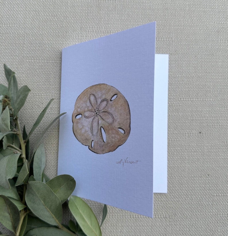 May include: A watercolor painting of a sand dollar on a light blue background. The sand dollar is brown and has a five-pointed star in the center. The artist's signature, "S. Vancut", is in the bottom right corner.