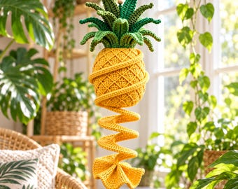 May include: A crocheted pineapple hanging decoration featuring a yellow textured fruit body with a green leafy top and a long yellow spiral tail extending downward. The item is suspended by a brown cord and includes the number 41 in the corner.