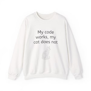 May include: A white long-sleeve crewneck sweatshirt featuring the black printed text My code works, my cat does not, positioned above a line-art illustration of a sitting cat. The garment has a ribbed neckline, cuffs, and hem.