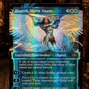 Può includere: Una carta collezionabile Magic: The Gathering intitolata Elspeth, Storm Slayer, con un'illustrazione olografica di un guerriero alato in armatura d'argento che impugna una spada luminosa. Il testo della carta descrive le abilità su sfondo scuro.