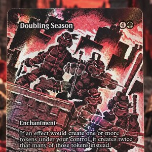 Könnte beinhalten: Eine rechteckige Sammelkarte mit dem Titel Doubling Season, die eine stilisierte Illustration von vier maskierten Schildkrötenfiguren in einer rot-schwarzen Stadtkulisse zeigt. Der Kartentext beschreibt einen Verzauberungseffekt und den Namen Kevin Eastman.