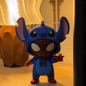 Könnte beinhalten: Eine blau-rote Vinylfigur eines Charakters in einem Spider-Man-Kostüm. Die Figur verfügt über eine texturierte blaue Kapuze mit großen Ohren, eine rote Maske mit schwarzem Spinnennetz-Muster, weiße Augen und ein schwarzes Spinnenemblem auf der Brust.