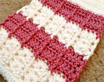 May include: A crocheted striped scarf in white and pink. The scarf is made with a textured stitch pattern.
