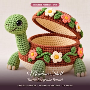 May include: A crochet turtle keepsake basket with a brown shell lid and cream base. The shell is decorated with white and pink flowers and green leaves. Text reads: CROCHET PATTERN, Meadow Shell Turtle Keepsake Basket, US TERMS.